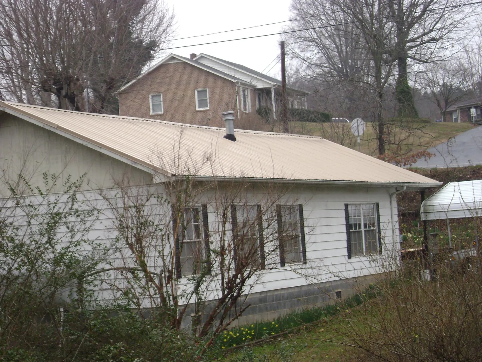 Tan metal roof on a white sided house set into a hillside — Commercial Roofing by Roofing Brothers in Milton