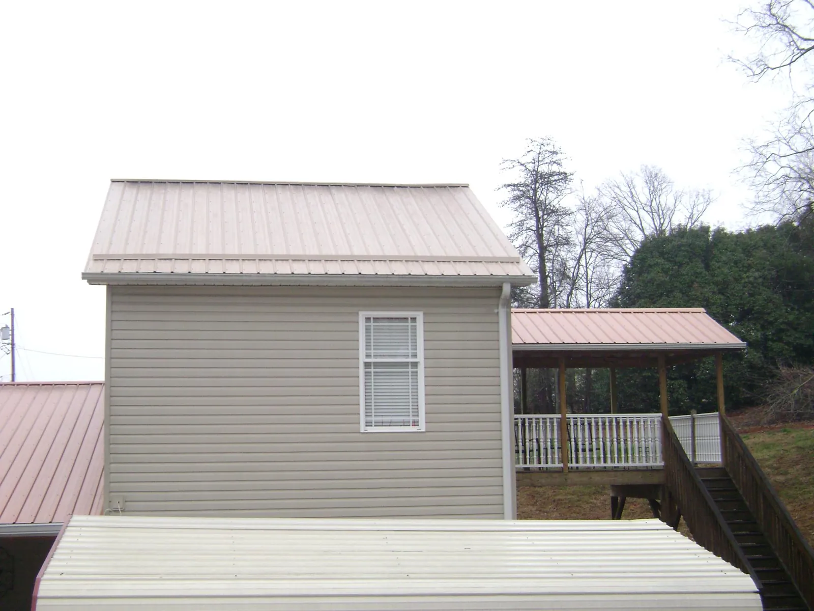 Tan metal roofs on a two story addition and attached porch, from a Roof Replacement job in Milton